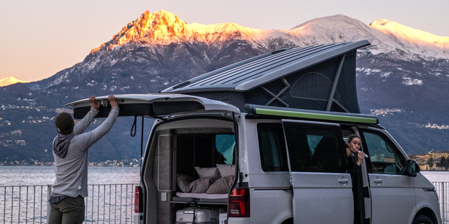Zwei Personen machen den Camper an einem Bergsee startklar für die Fahrt