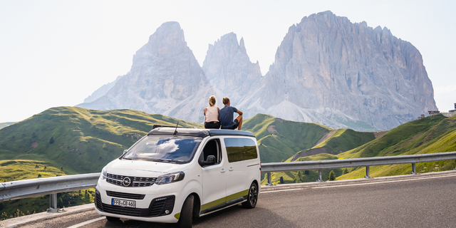 Zwei Personen sitzen auf einem Camper in den Dolomiten
