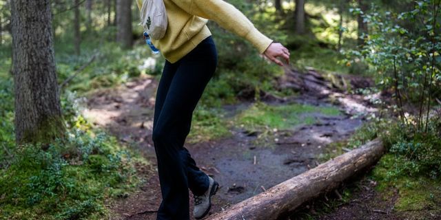 Frau mit Bauchtasche spaziert in Wanderkleidung auf Baumstamm