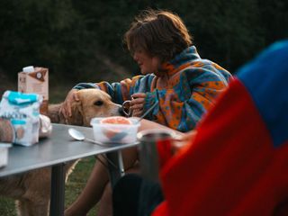 Frau beim Essen am Campingtisch mit Hund